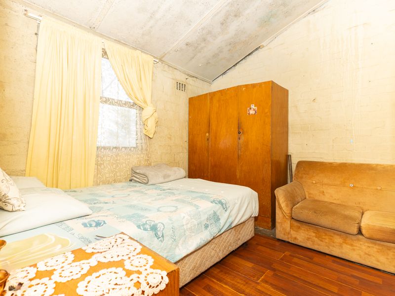 A bedroom featuring timber flooring, exposed brick walls, and a sloped ceiling with visible signs of water damage and wear.
