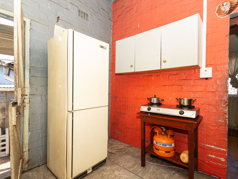 A basic kitchen area featuring exposed brick walls, wall-mounted cabinetry, and tiled flooring, requiring significant cosmetic updates and modernization.