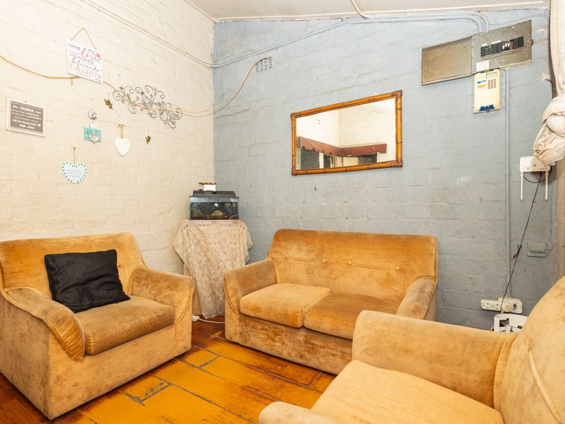 A living area featuring exposed brick walls, timber flooring, and visible electrical infrastructure, offering potential for cosmetic updates and modernization.