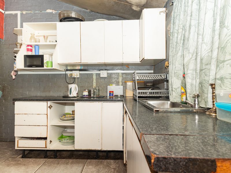 A dated kitchen featuring exposed brick walls, laminate countertops, and basic cabinetry in need of significant renovation and cosmetic updates.