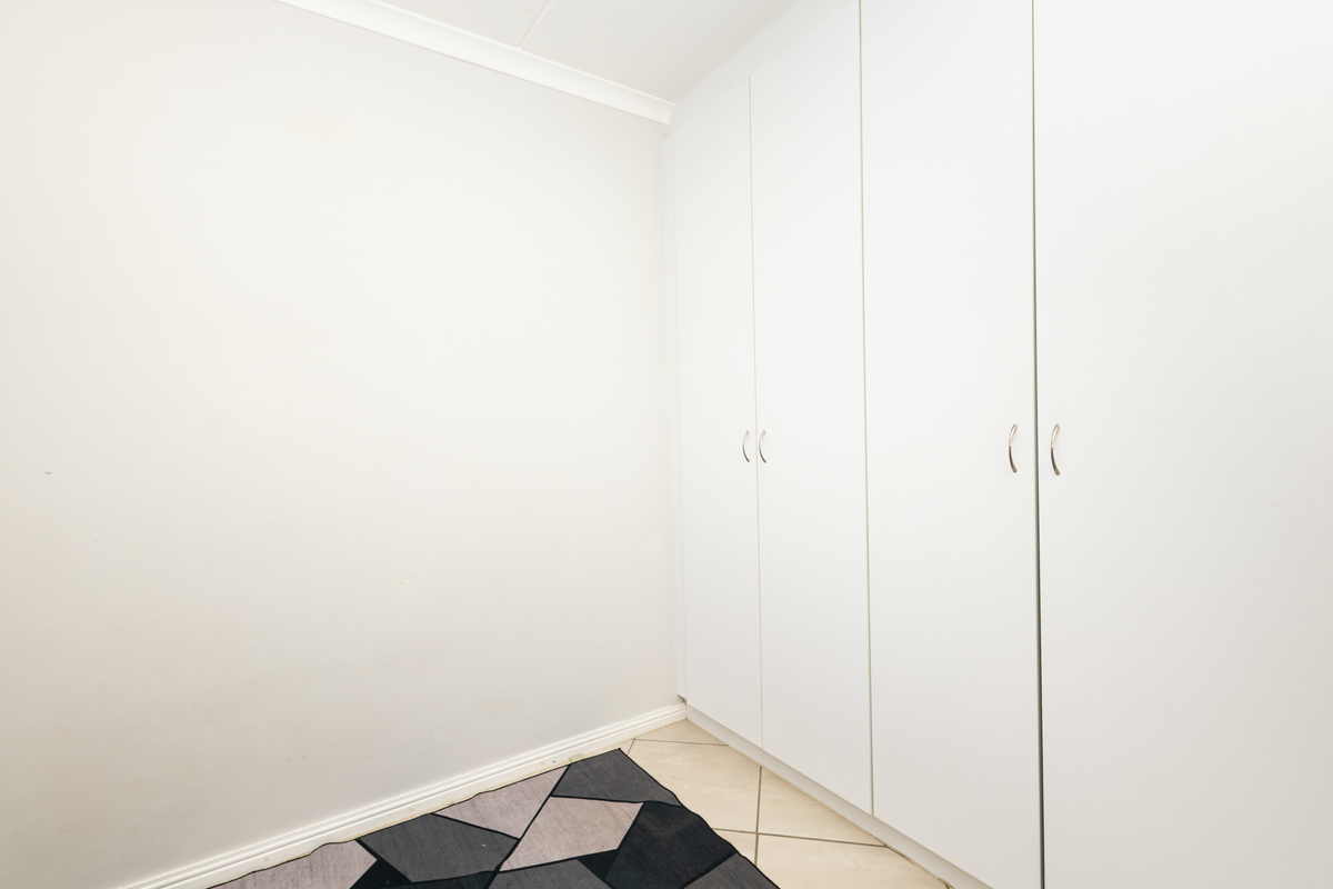 A clean, empty bedroom featuring neutral tiled flooring and ample built-in cupboard storage with white cabinetry.