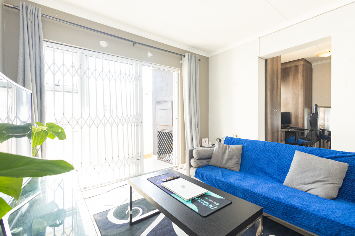 Living room featuring tiled flooring, a sliding glass door with security gate, and built-in cabinetry in the adjacent alcove.