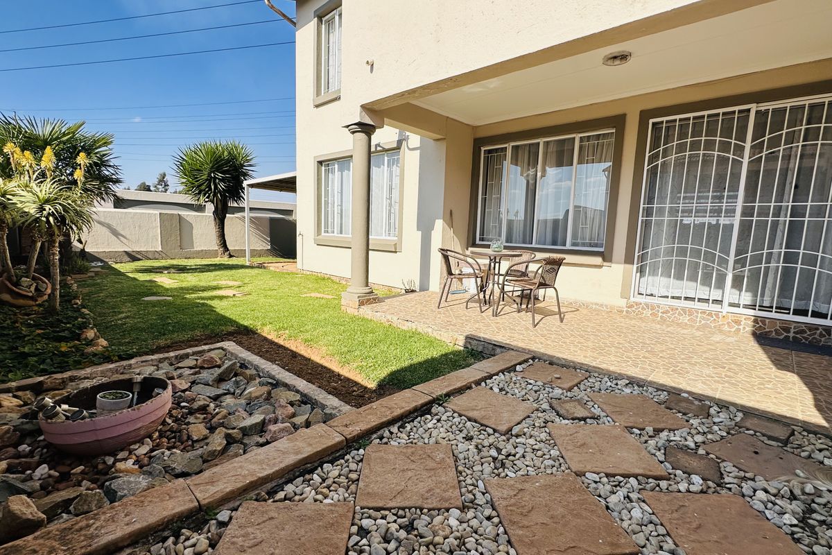 A well-maintained rear exterior featuring a tiled patio, security gates, and a landscaped garden with stone pathways and lawn.