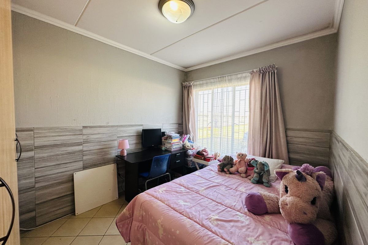 A bedroom featuring tiled flooring, partial wall tiling, and a window with security bars, providing a functional space with natural light.