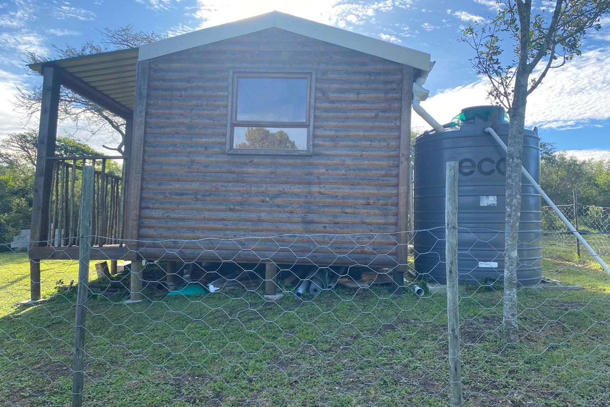 A rustic log cabin structure featuring a raised timber deck and an integrated water storage tank, situated on a fenced residential plot.