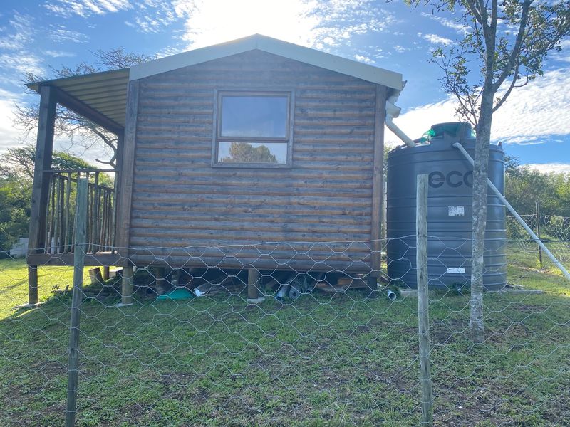 A rustic log cabin structure featuring a raised timber deck and an integrated water storage tank, situated on a fenced residential plot.