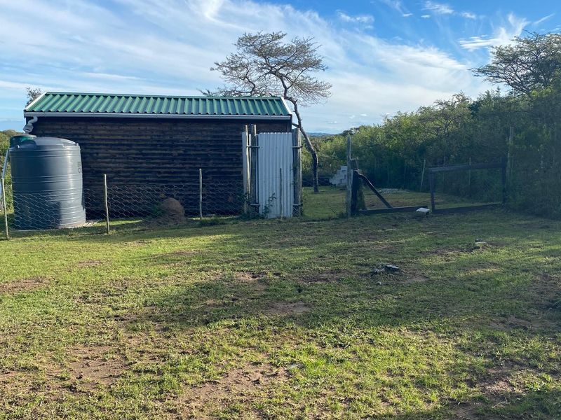 A view of a rear garden area featuring a small timber shed, a water tank, and wire fencing on a grassy plot.