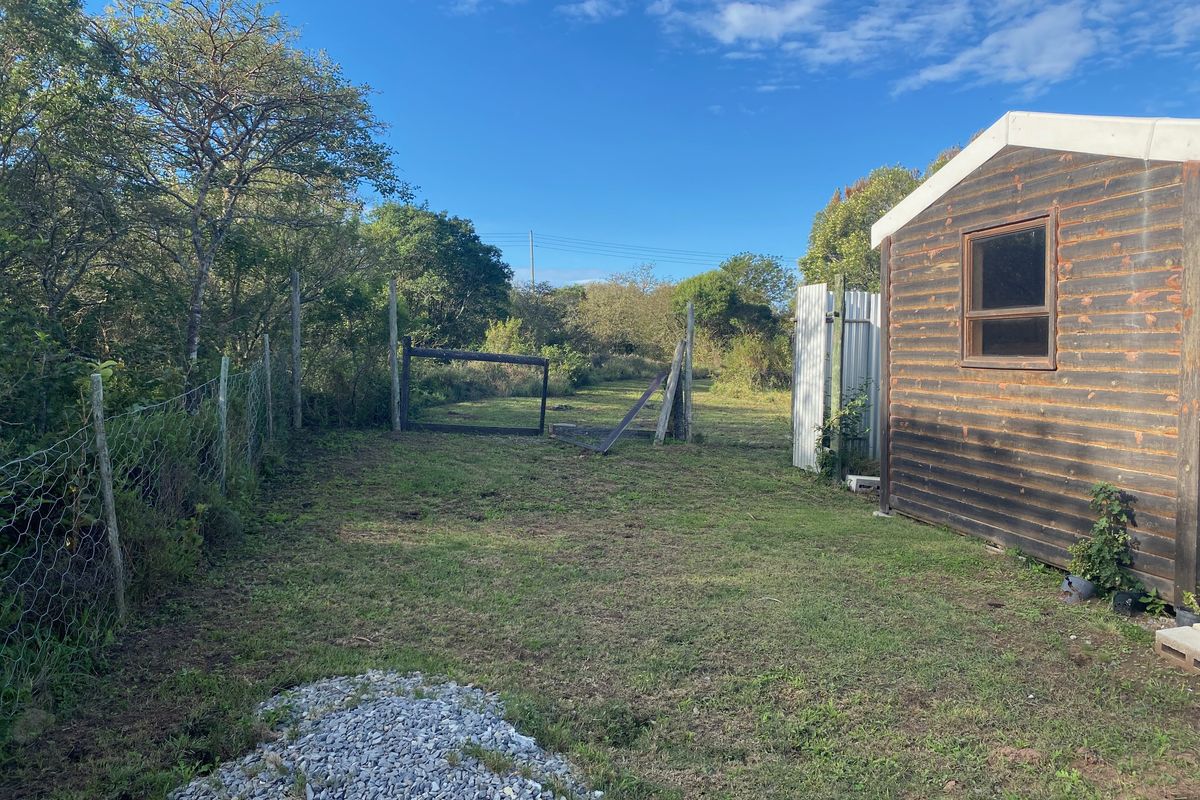 A view of a residential garden plot featuring a timber shed, wire fencing, and a damaged gate, set against a natural landscape.