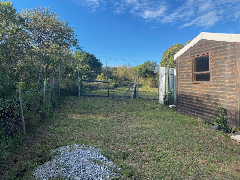 A view of a residential garden plot featuring a timber shed, wire fencing, and a damaged gate, set against a natural landscape.