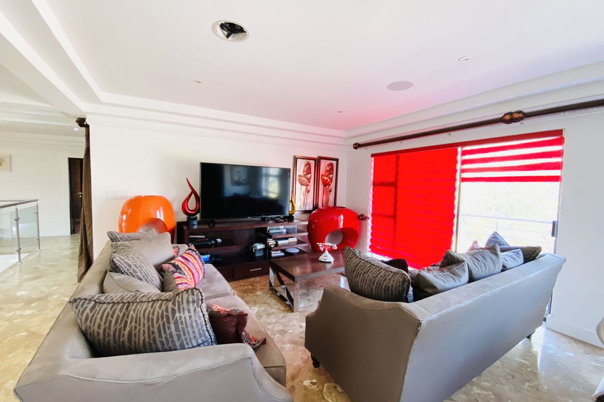 A spacious living room featuring polished marble flooring, recessed ceiling lighting, and large windows with vibrant red blinds.