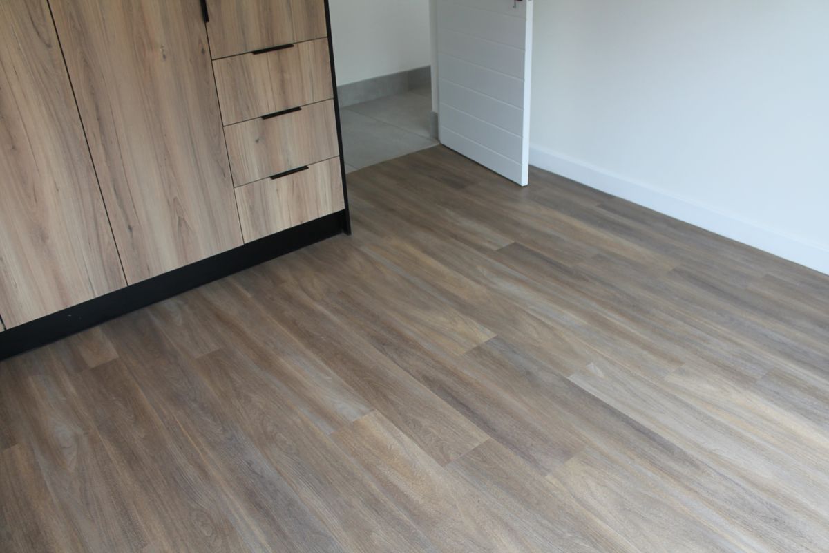 A clean, modern bedroom space featuring wood-look laminate flooring and built-in cabinetry with a neutral finish.