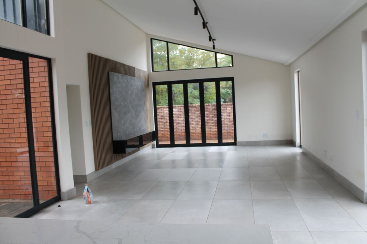 Spacious open-plan living area featuring large stacker doors, raked windows, tiled floors, and a modern feature wall with built-in media cabinetry.