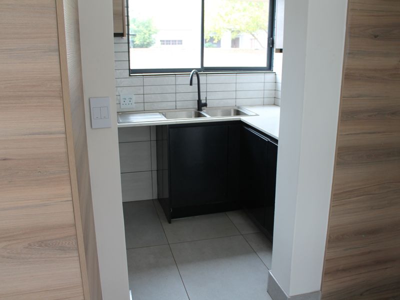 A compact, modern scullery featuring dark cabinetry, a double sink with a black mixer tap, and neutral tiled splashbacks.