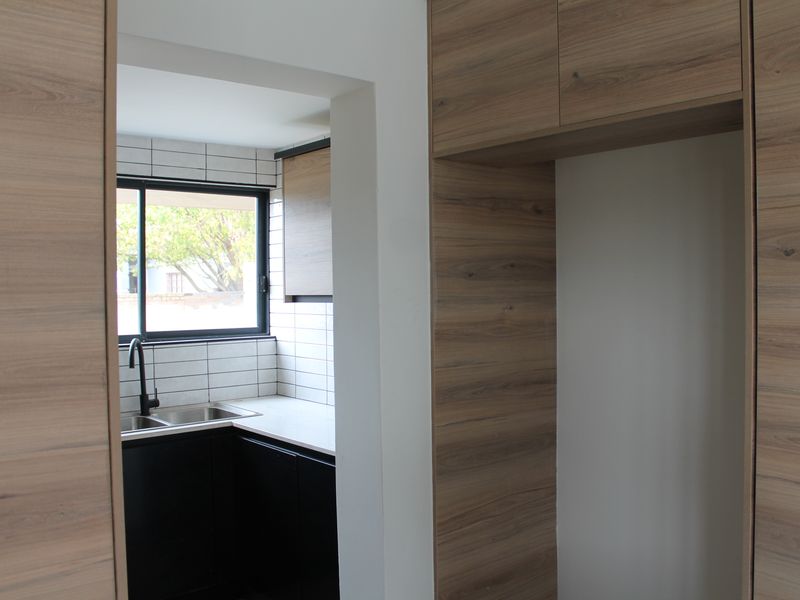 A modern, clean scullery area featuring wood-look cabinetry, a stainless steel sink with a black mixer tap, and white tiled splashbacks.