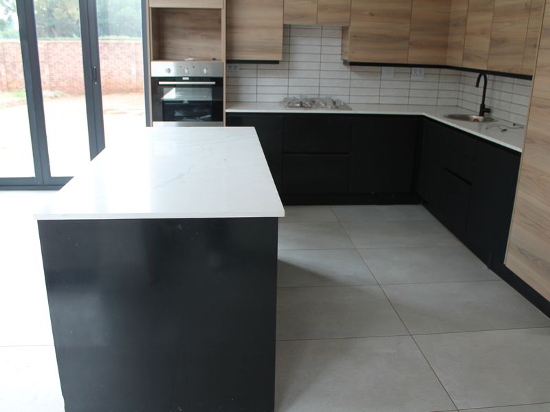Modern kitchen featuring a central island, two-tone cabinetry, stone countertops, built-in oven, gas hob, and large format floor tiles with direct access to the outdoors.
