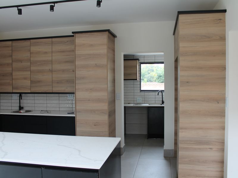 Modern kitchen featuring wood-grain cabinetry, stone countertops, a central island, and a separate scullery area with subway tile backsplash.