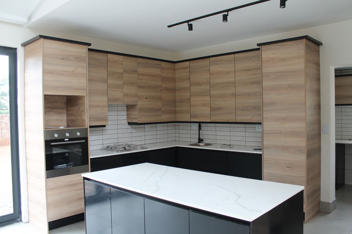 Modern kitchen featuring wood-grain cabinetry, black lower cabinets, a central island with a stone countertop, built-in oven, and subway tile backsplash.