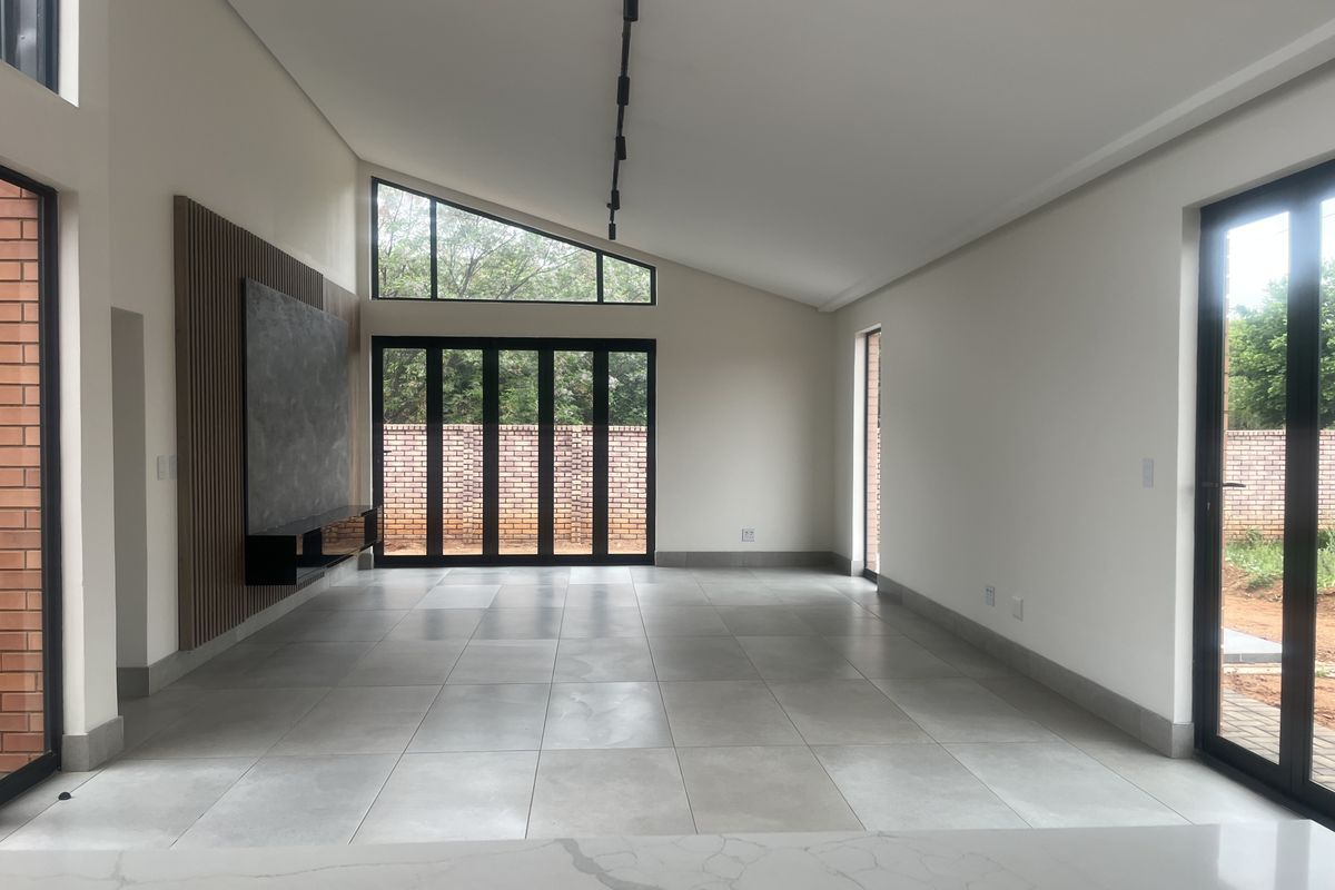 Spacious open-plan living area featuring large format floor tiles, a modern slatted timber feature wall with built-in console, and expansive aluminium stacker doors.