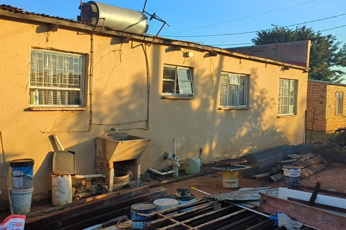 Rear exterior view of the property showing a concrete wash basin, solar water heater, and basic masonry walls requiring maintenance.