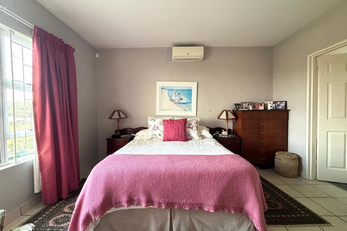 A well-maintained bedroom featuring tiled flooring, a wall-mounted air conditioning unit, and a window with security bars.