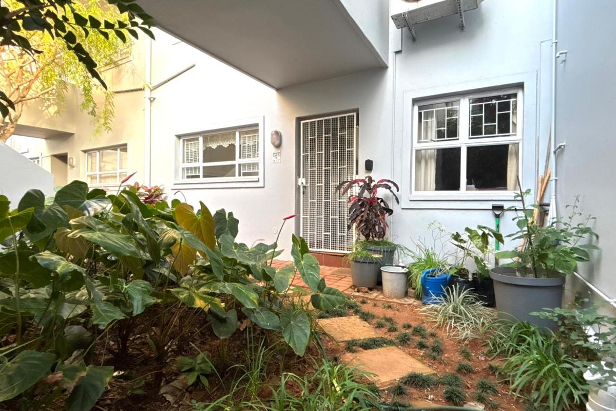 Ground floor apartment entrance featuring a private garden area, security gate, and external air conditioning unit.