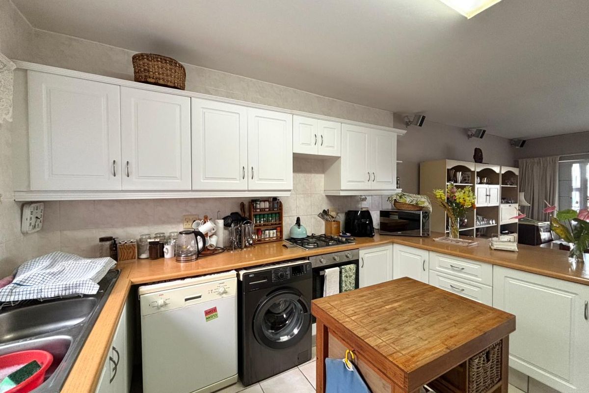 Functional kitchen featuring white cabinetry, wood-look laminate countertops, integrated gas hob, oven, and dedicated space for laundry appliances.