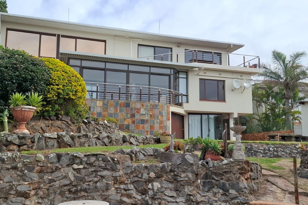Rear view of a multi-level house featuring stone retaining walls, a balcony with stainless steel railings, and large sliding glass doors.