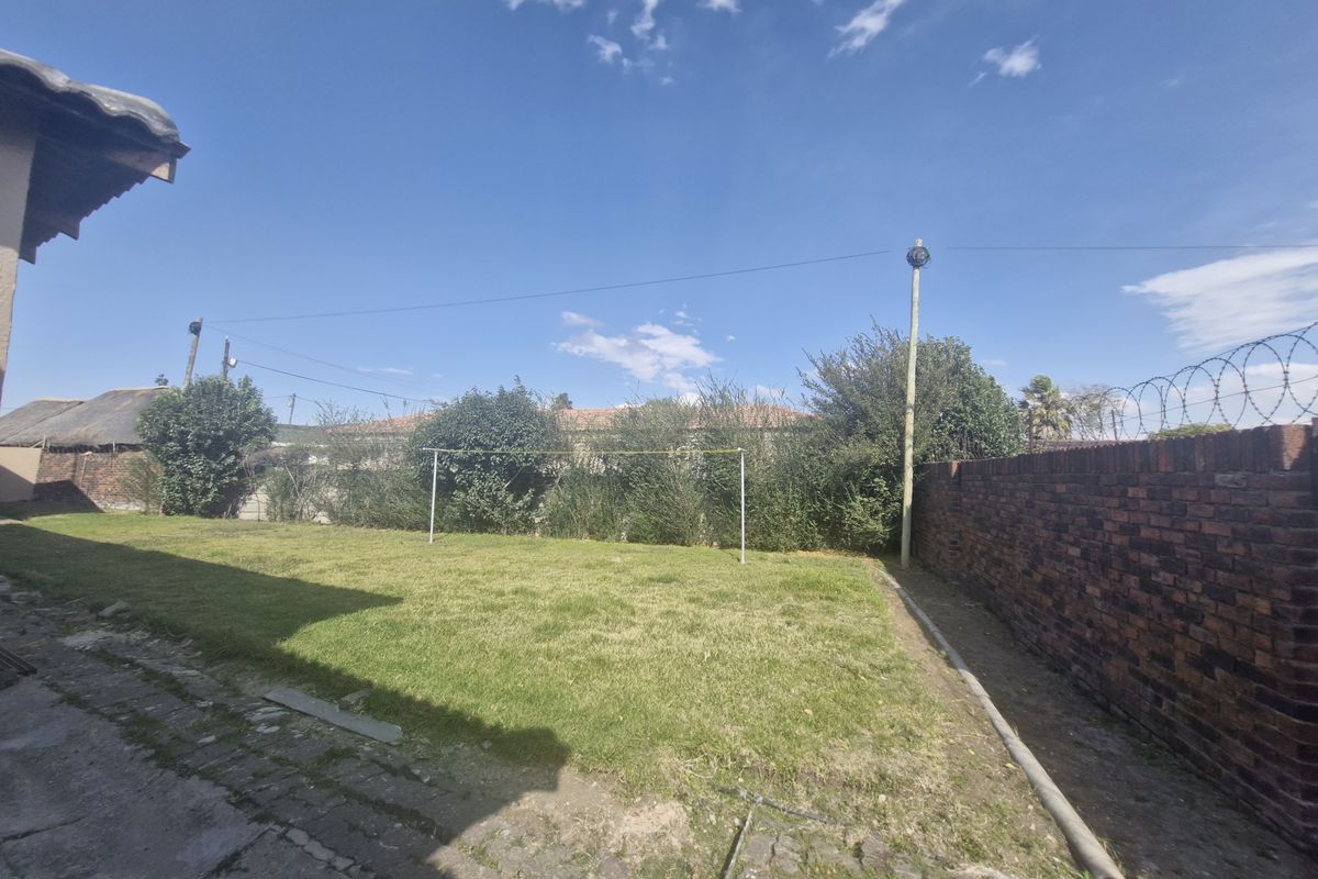 A rear garden area featuring a lawn, concrete paving, and a brick boundary wall topped with security razor wire.