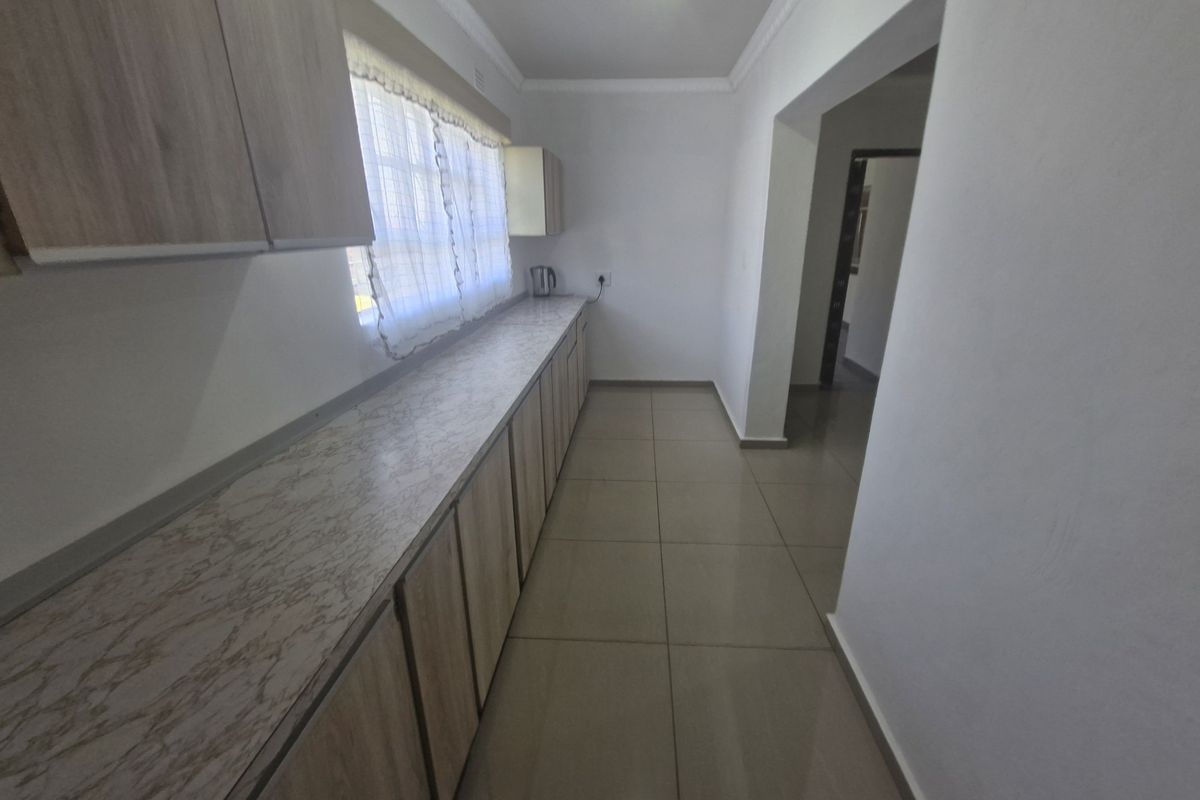 A clean, empty kitchen featuring light wood-look cabinetry, marble-effect laminate countertops, and neutral floor tiles, offering a functional and well-maintained workspace.