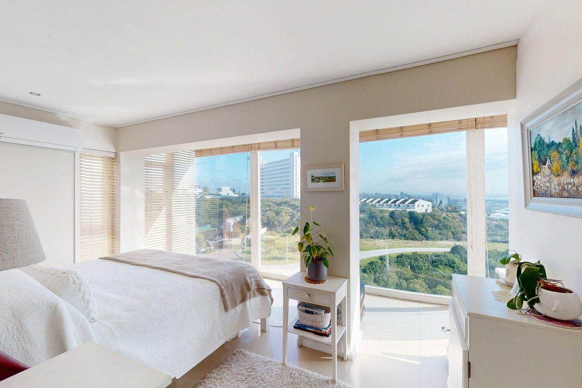 Bright and airy bedroom featuring large floor-to-ceiling windows with expansive views, tiled flooring, and a wall-mounted air conditioning unit.