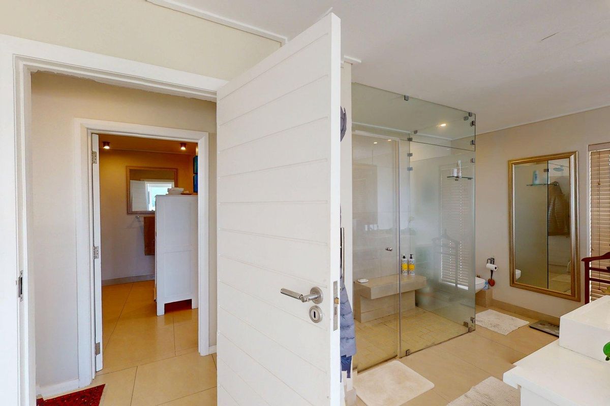 A well-lit bathroom featuring a spacious glass-enclosed shower with a built-in bench, tiled flooring, and a large wall-mounted mirror.