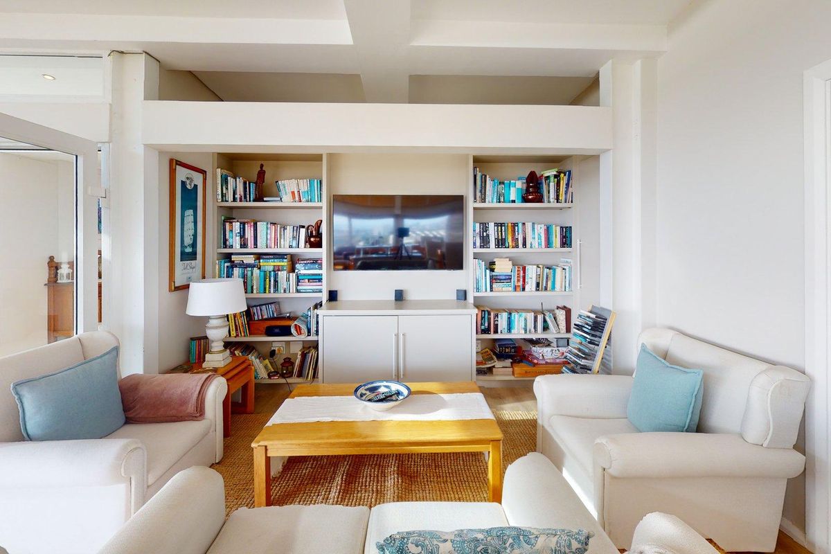 A well-maintained living room featuring custom built-in shelving and cabinetry surrounding a central television area, complemented by architectural ceiling beams.