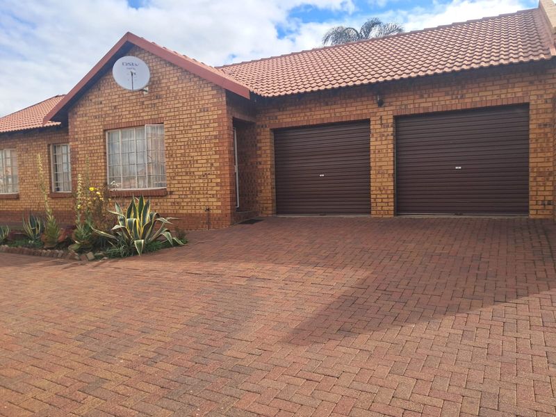 Front elevation of a facebrick townhouse featuring a double garage with roll-up doors and a paved driveway.
