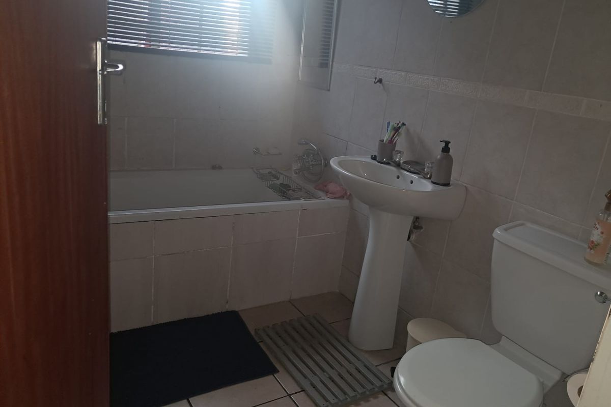A functional bathroom featuring a pedestal basin, built-in bathtub, and toilet with neutral wall and floor tiling.