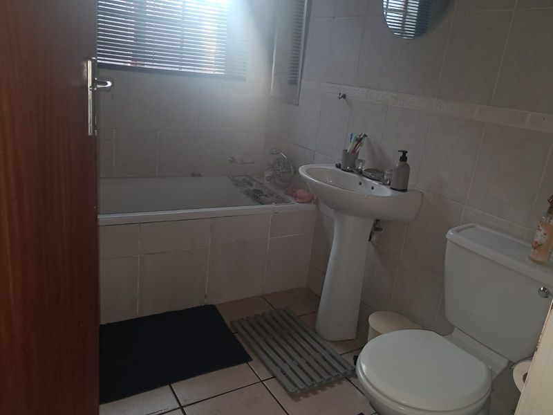 A functional bathroom featuring a pedestal basin, built-in bathtub, and toilet with neutral wall and floor tiling.