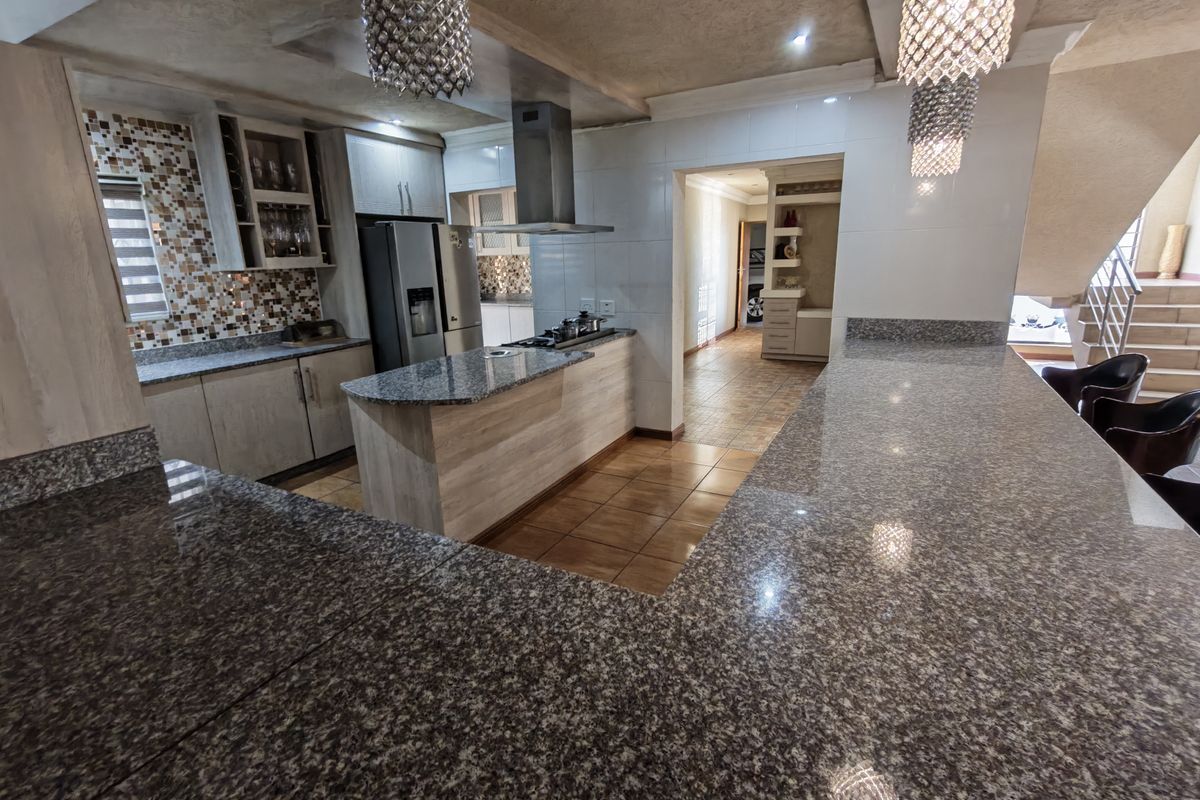 Modern kitchen featuring granite countertops, extensive built-in cabinetry, a gas hob with extractor fan, and stylish pendant lighting, flowing into an open-plan living area.
