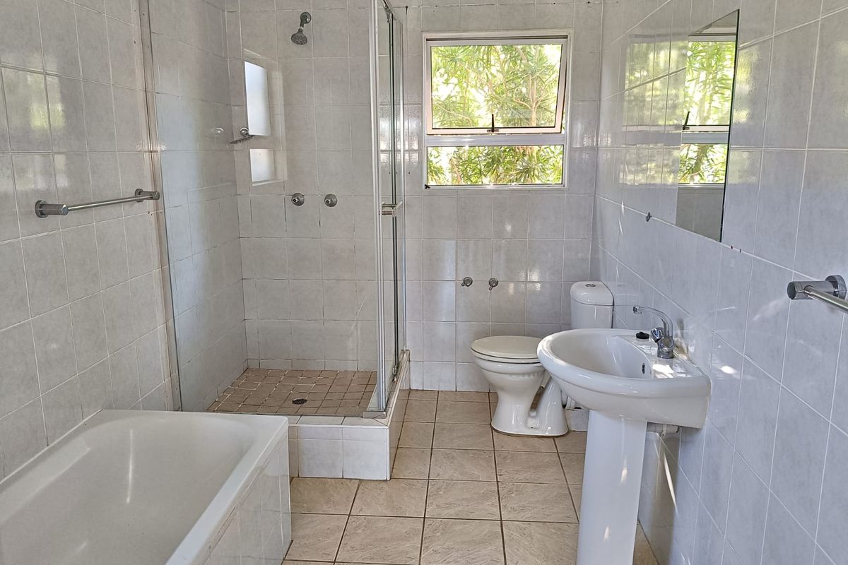 A functional bathroom featuring a separate shower enclosure, bathtub, pedestal basin, and toilet, finished with neutral wall and floor tiling.