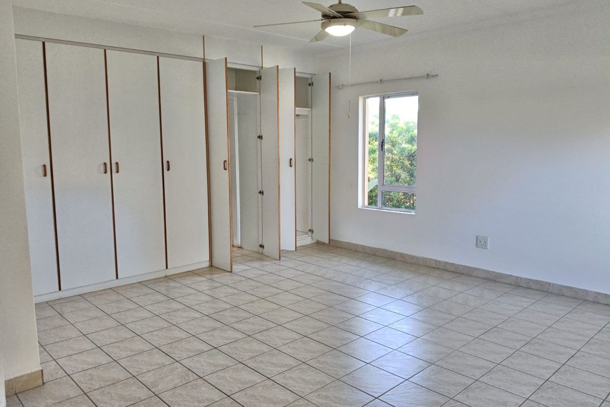 Spacious bedroom featuring neutral tiled flooring, extensive built-in cupboard storage, and a ceiling fan, offering a clean and versatile living space.