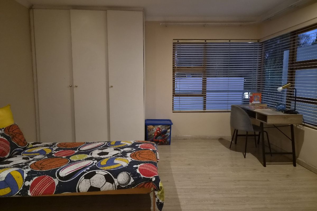 A bedroom featuring built-in cupboards, laminate flooring, and large windows with fitted blinds, providing ample natural light.