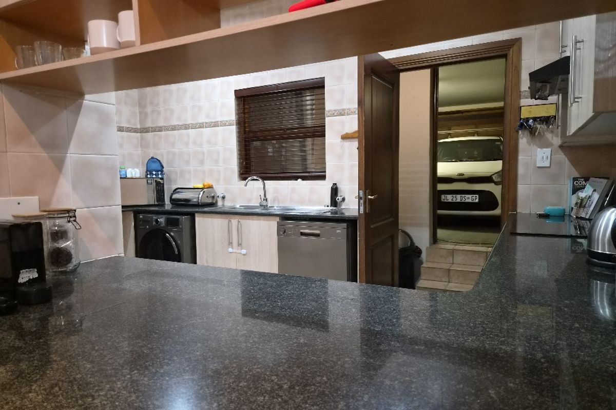 A functional kitchen featuring granite countertops, tiled splashbacks, and integrated cabinetry, with direct access to the garage area.