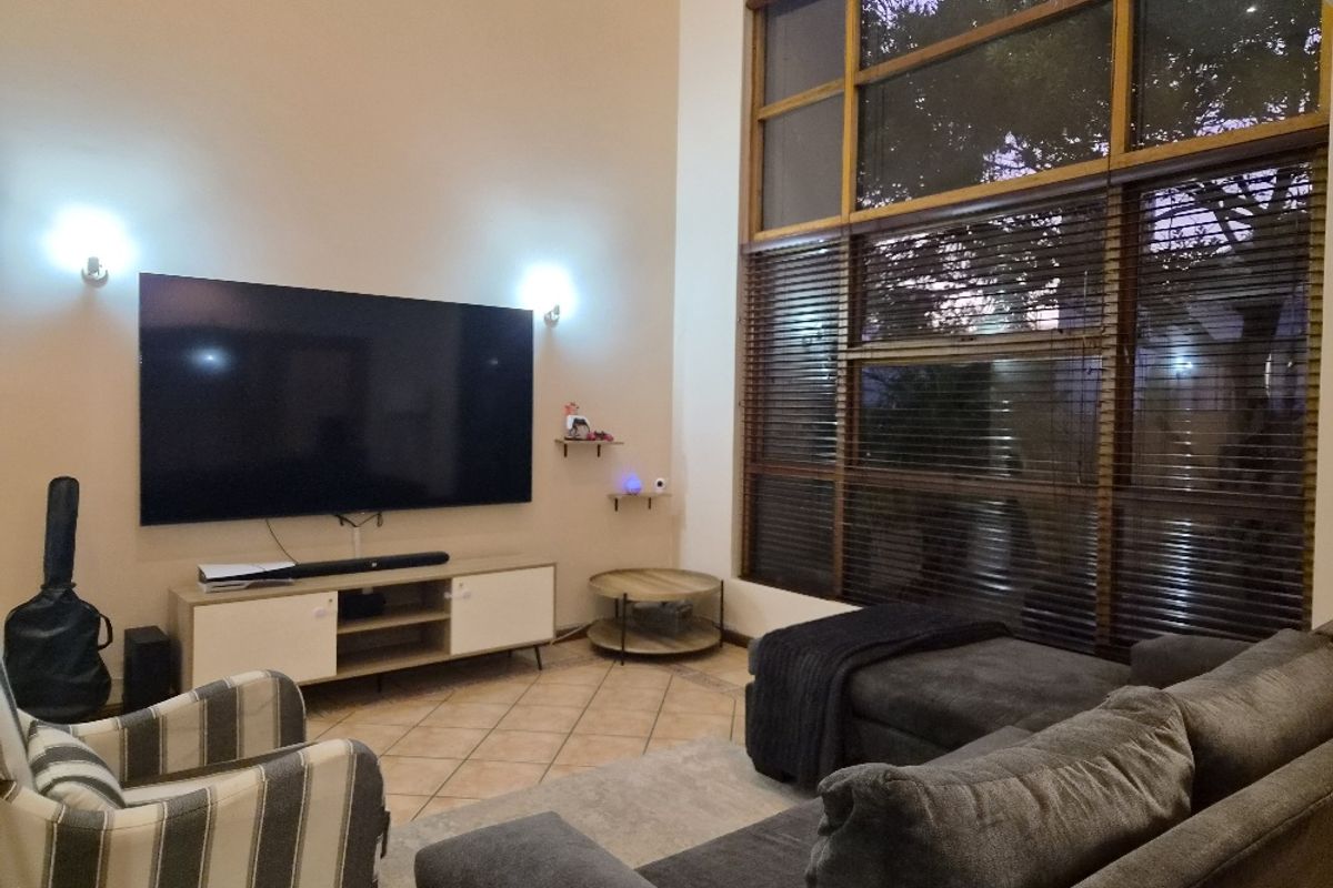 Spacious living room featuring high ceilings, large floor-to-ceiling windows with wooden blinds, and tiled flooring.