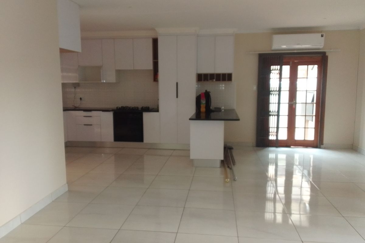Spacious open-plan living area featuring a modern kitchen with white cabinetry, black granite countertops, built-in appliances, and direct access to the outdoors.