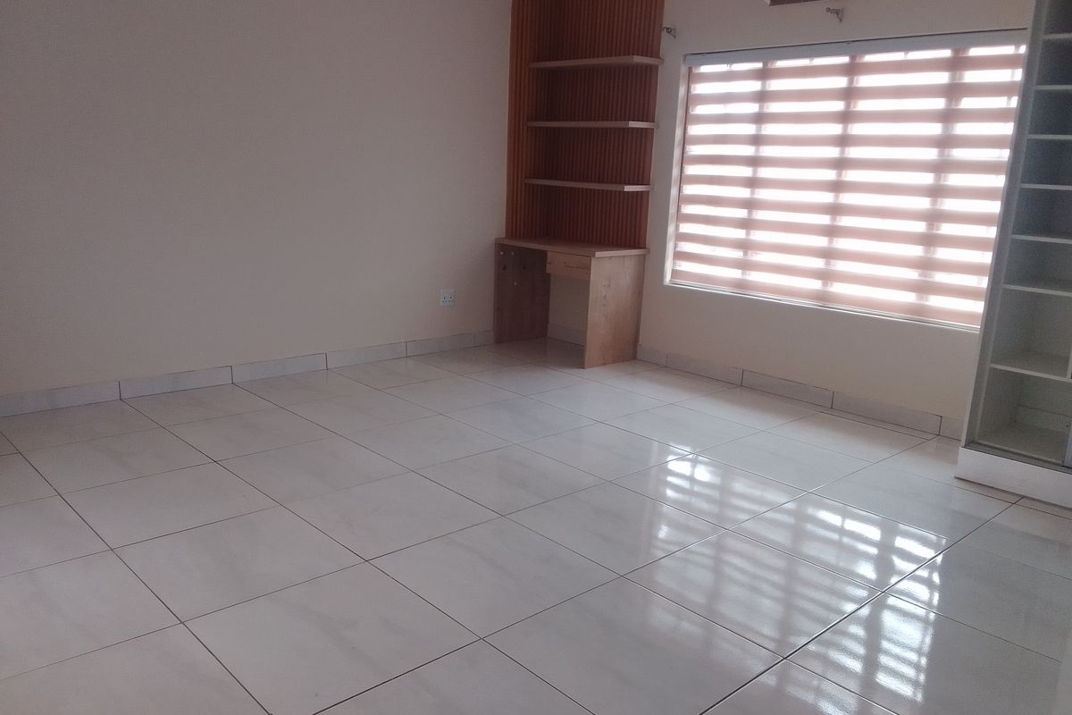 A bright, empty bedroom featuring polished tile flooring, a built-in desk with shelving, an air conditioning unit, and modern window blinds.