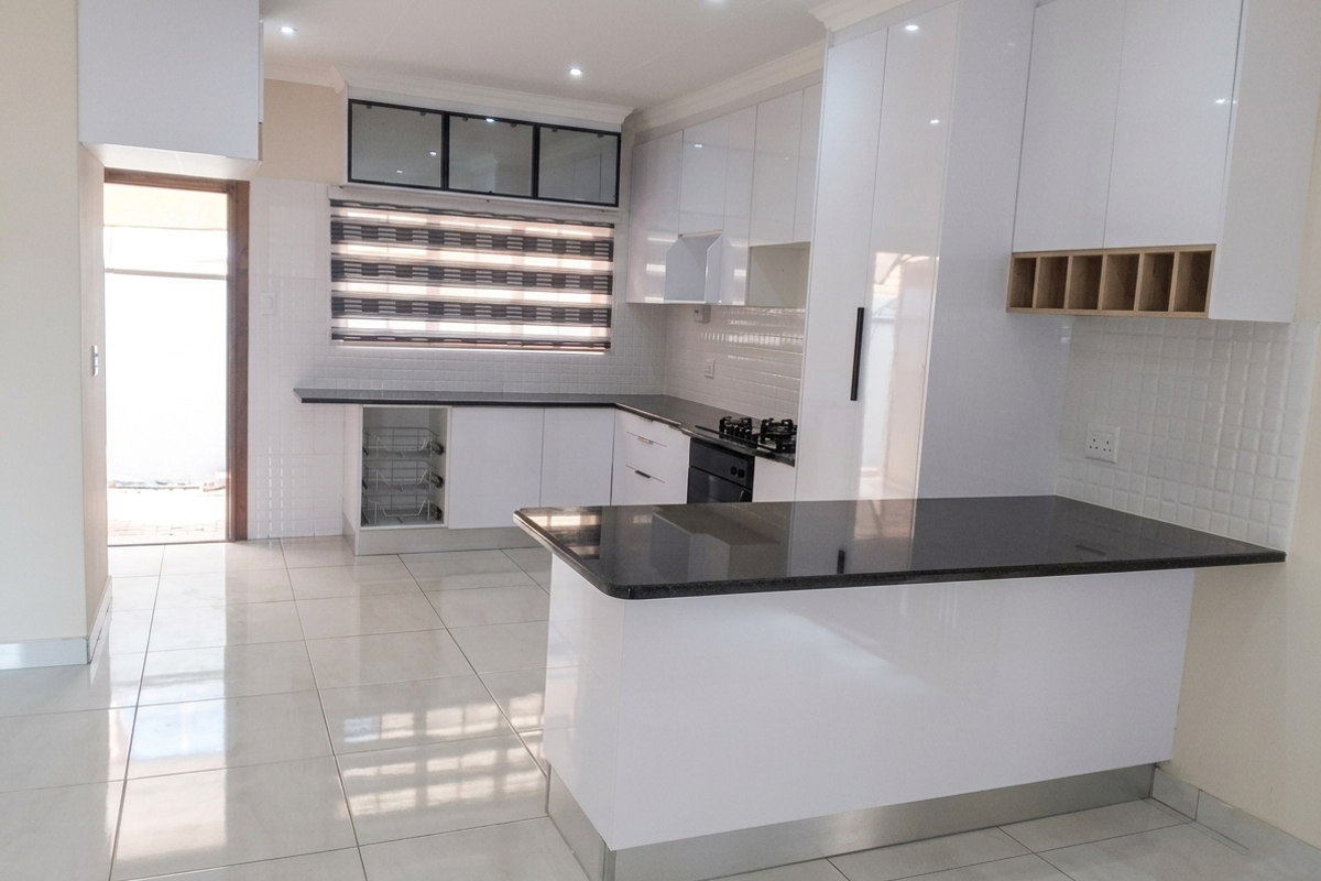 Modern kitchen featuring high-gloss white cabinetry, granite countertops, a gas hob, built-in oven, and sleek tiled flooring in a bright, open layout.
