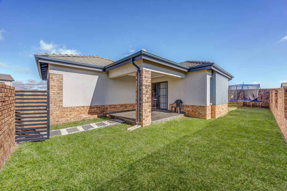 Rear view of the property featuring a covered patio, brick exterior walls, a well-maintained lawn, and secure boundary walling.