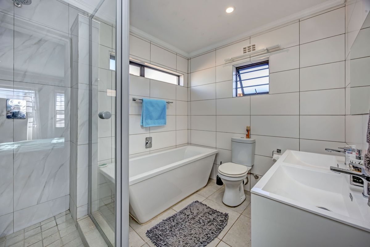 Modern bathroom featuring a freestanding bathtub, glass-enclosed shower, dual vanity basin, and clean white ceramic wall tiling.