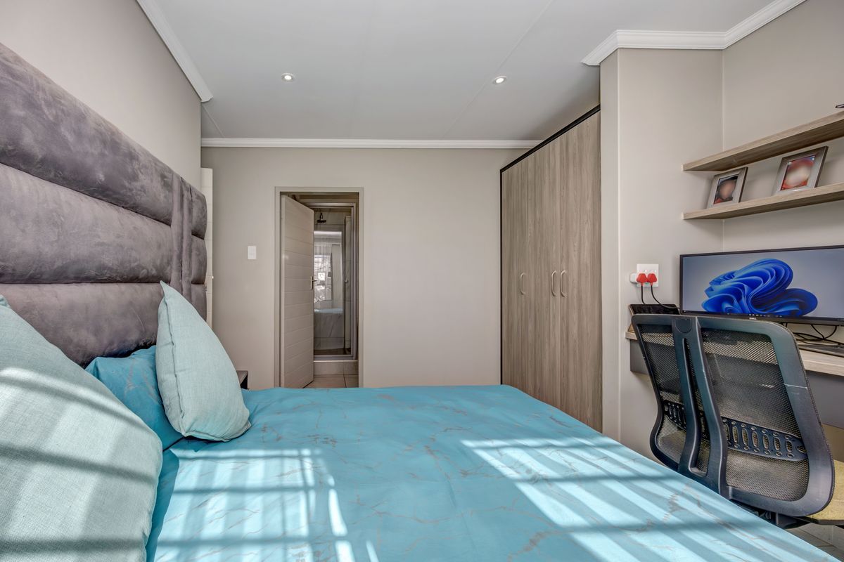 A well-maintained bedroom featuring a built-in wardrobe, integrated desk space with shelving, and recessed lighting, with an adjoining en-suite bathroom.