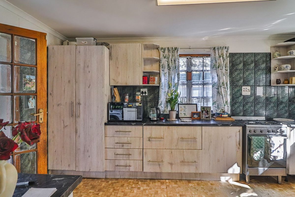 A functional kitchen featuring light wood-look cabinetry, dark countertops, a gas stove, and a tiled backsplash, with direct access to the exterior.