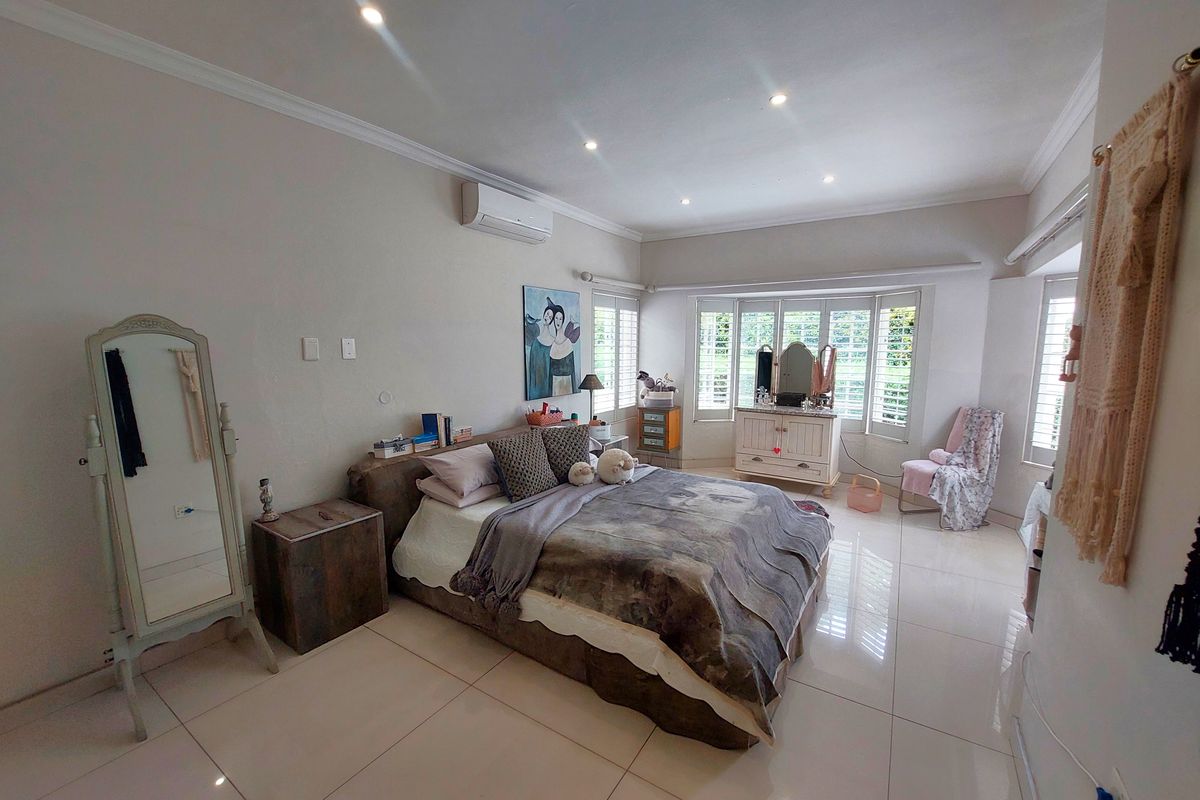Spacious bedroom featuring large porcelain floor tiles, recessed downlighting, a split-system air conditioner, and a bay window fitted with plantation shutters.