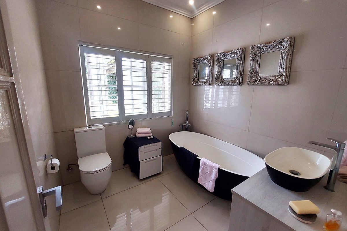 Modern bathroom featuring a sleek freestanding bathtub, contemporary vessel sink, floor-to-ceiling tiling, and plantation shutters for natural light control.